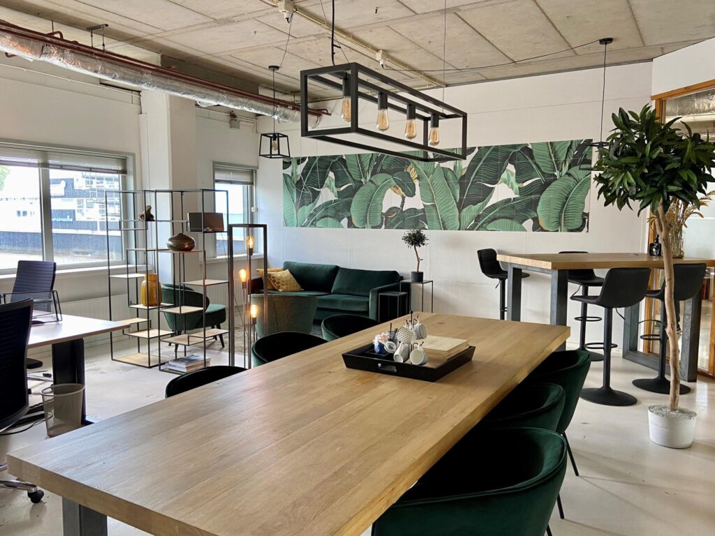 Moderne kantoorruimte aan de Anthony Fokkerweg met houten tafels, groene meubels en een tropisch wandpaneel.